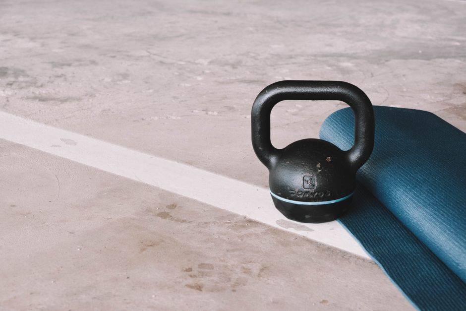 Kettlebell and blue yoga mat on a concrete floor in an indoor gym setting.